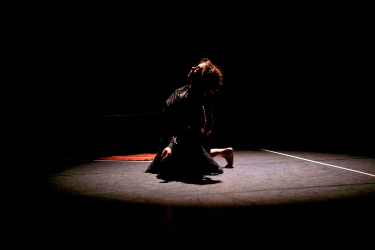 一名舞蹈演员在一间黑暗的房间里，在聚光灯的照耀下在地板上表演。