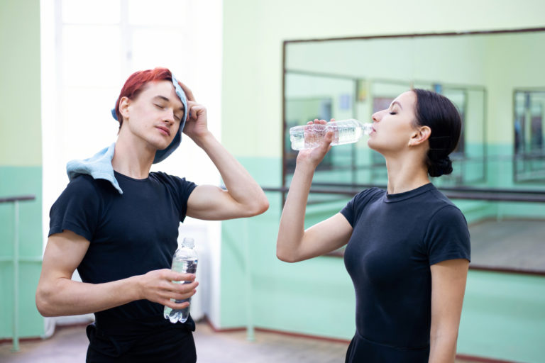 一个年轻的男舞者和一个年轻的女舞者在工作室的课堂上喝水。