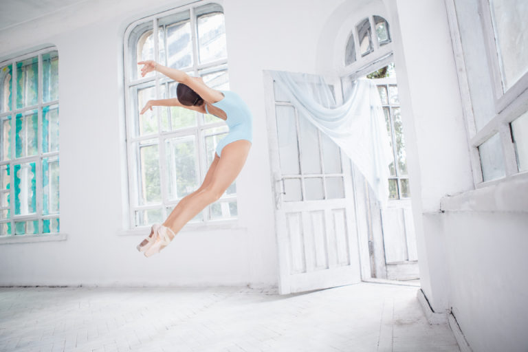年轻的现代芭蕾舞者在白色房间背景上跳跃或飞行