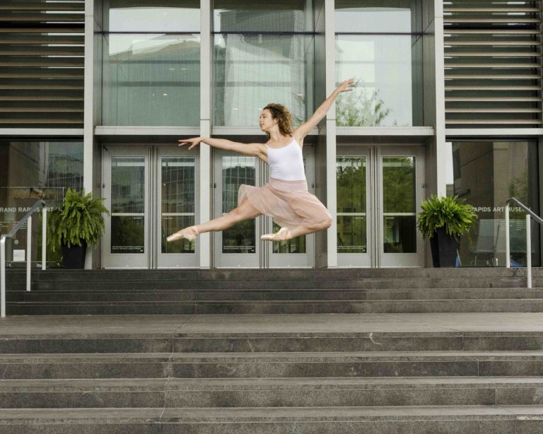 芭蕾舞演员在表演艺术设施前跳跃的画面