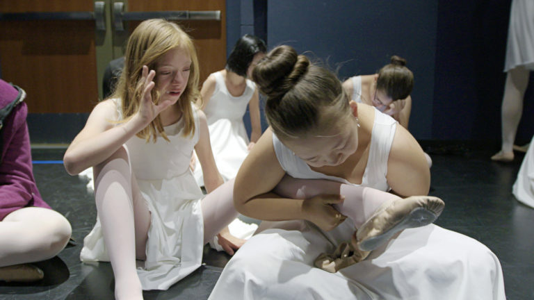年轻的学生帮她的同伴穿芭蕾舞鞋